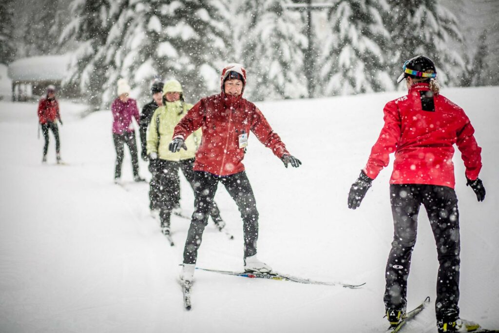 5 women in red jackets with black snowpants cross country skiing during a light snowfall